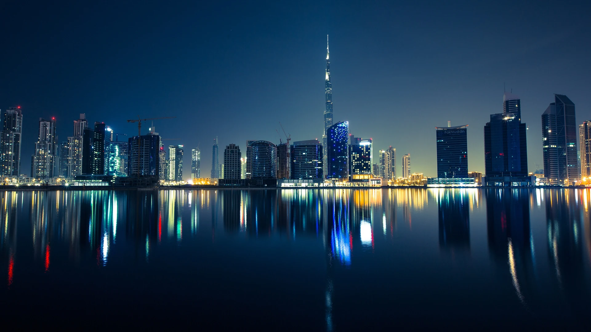 Downtown Dubai's skyline reflected in water at night, with the illuminated Burj Khalifa rising above the hotel towers